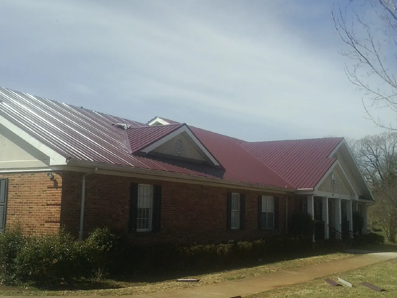 Red metal roof with gabled entries on a long brick building, from a Hail Damage Roof Repair job in Saugerties