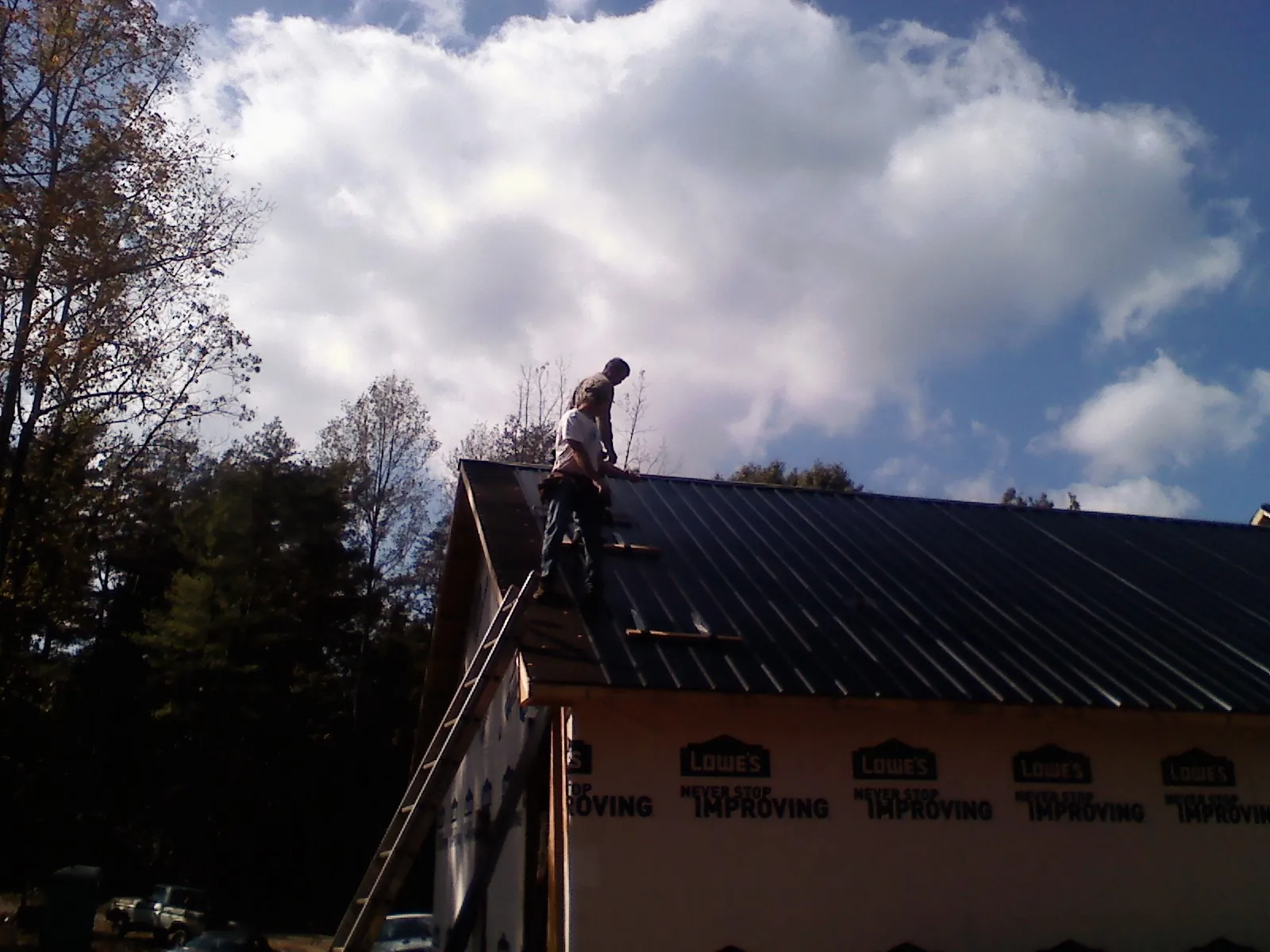 Roofer fastening dark metal panels high against a cloudy sky, from a Roof Inspection job in Saugerties