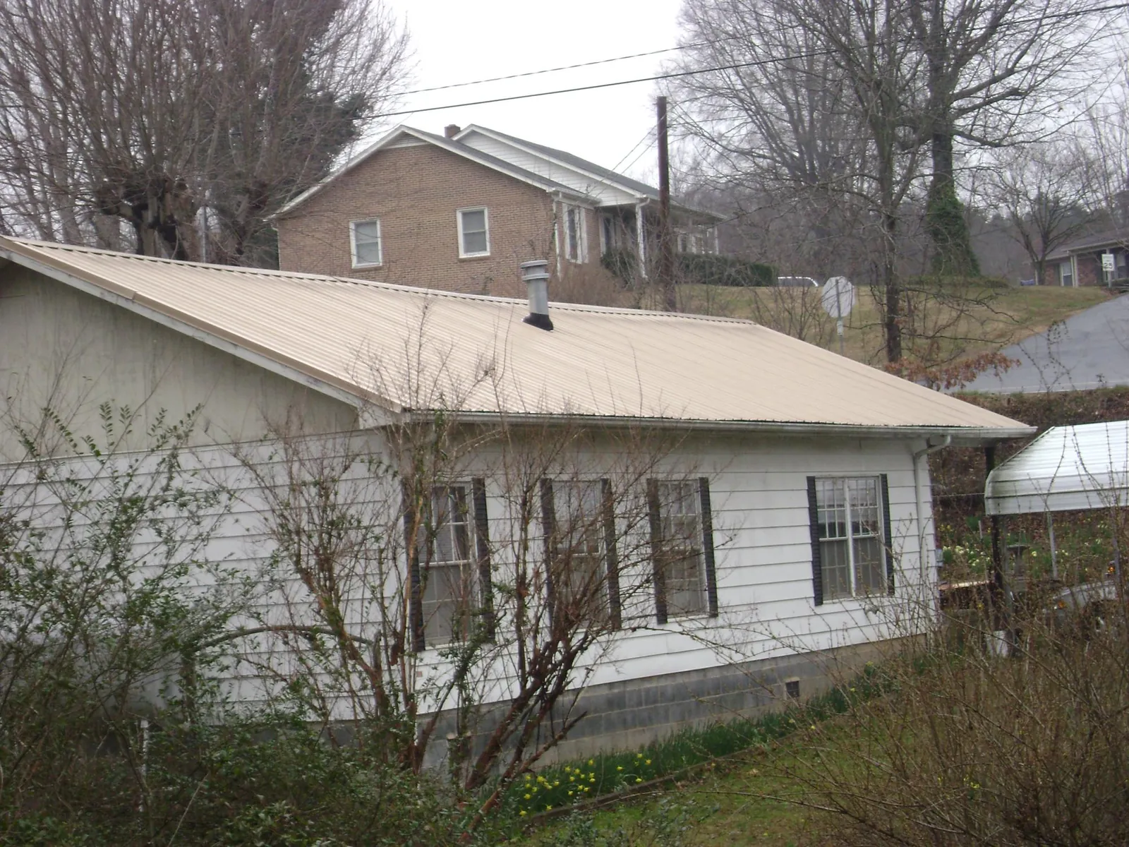 Tan metal roof on a white sided house set into a hillside — Commercial Roofing by Roofing Brothers in Saugerties
